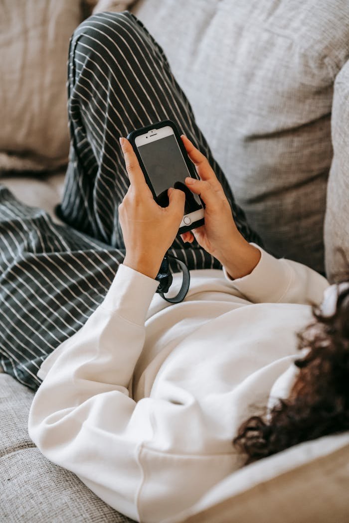 Woman in cozy clothes using smartphone on couch during leisure time.